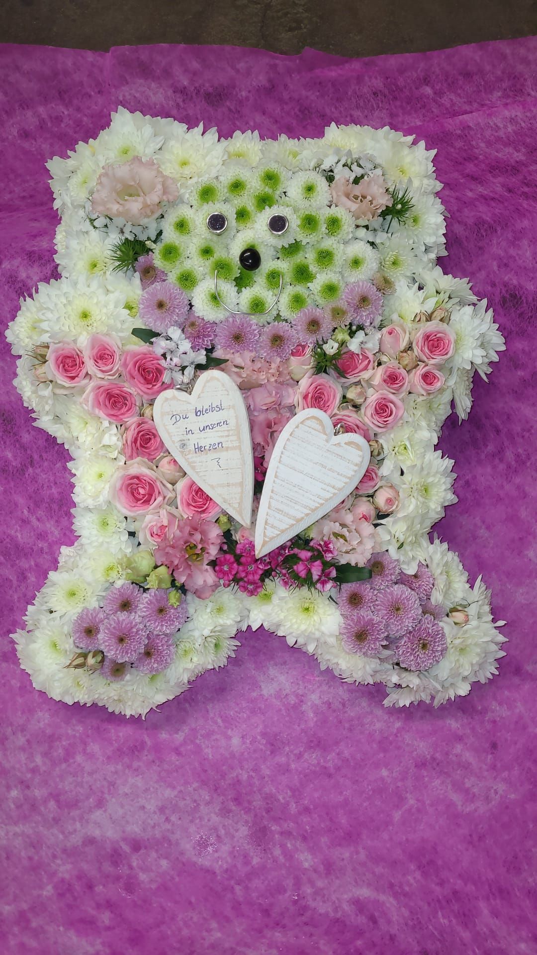 Ein Teddybär aus Blumen und einem Herzen auf violettem Untergrund.