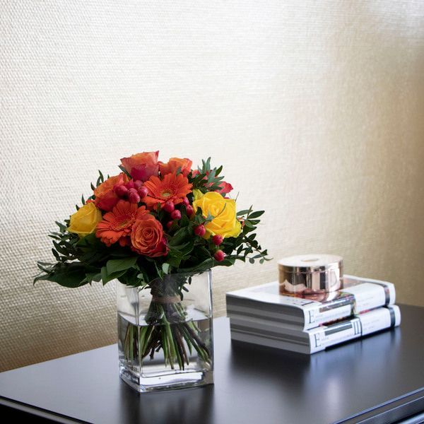 Eine Vase mit Blumen steht auf einem Tisch neben einem Stapel Bücher.