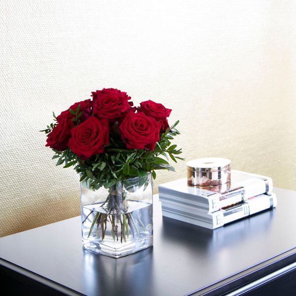 Eine Vase mit roten Rosen steht auf einem Tisch neben einem Stapel Bücher