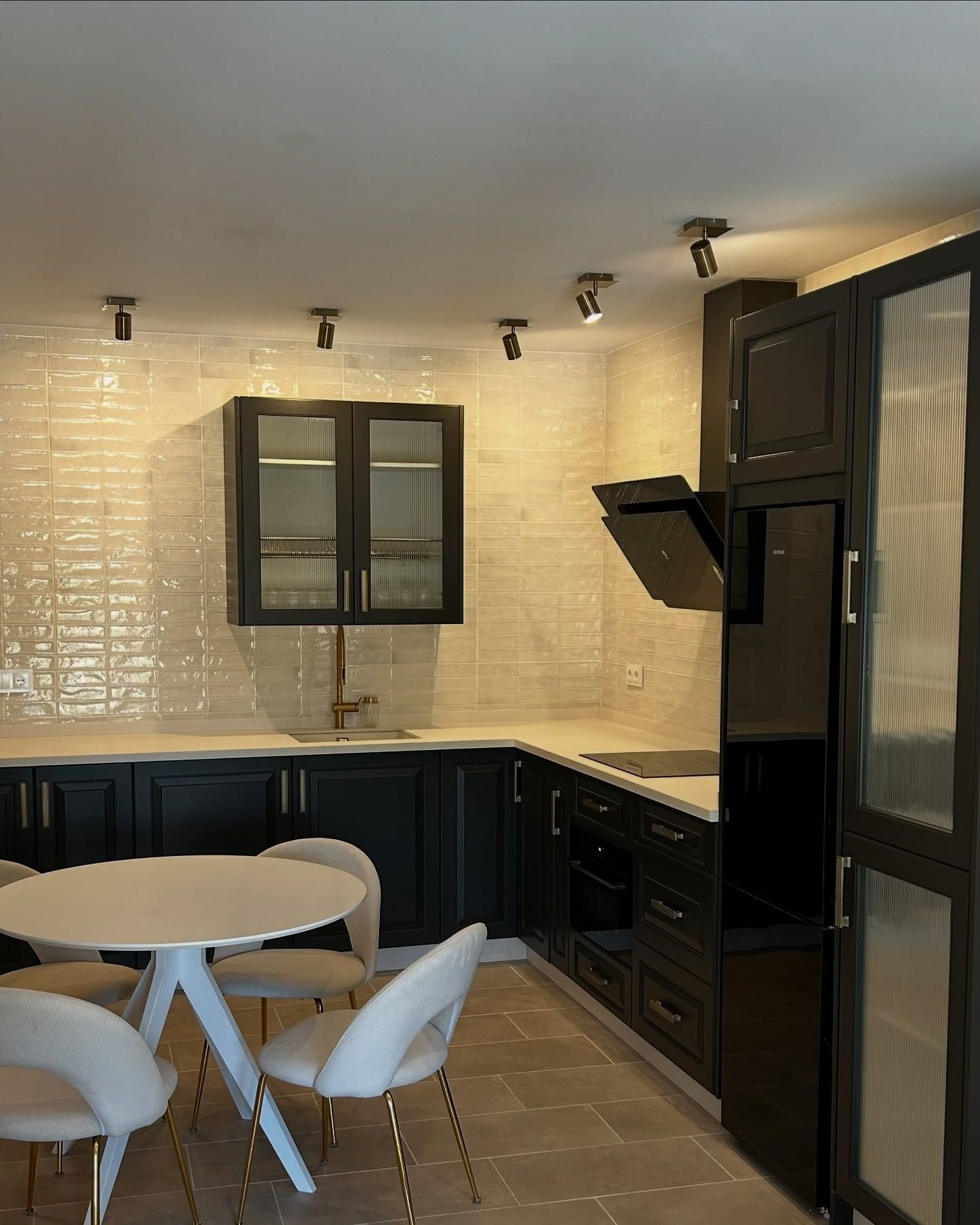 Una cocina con gabinetes negros y sillas blancas.