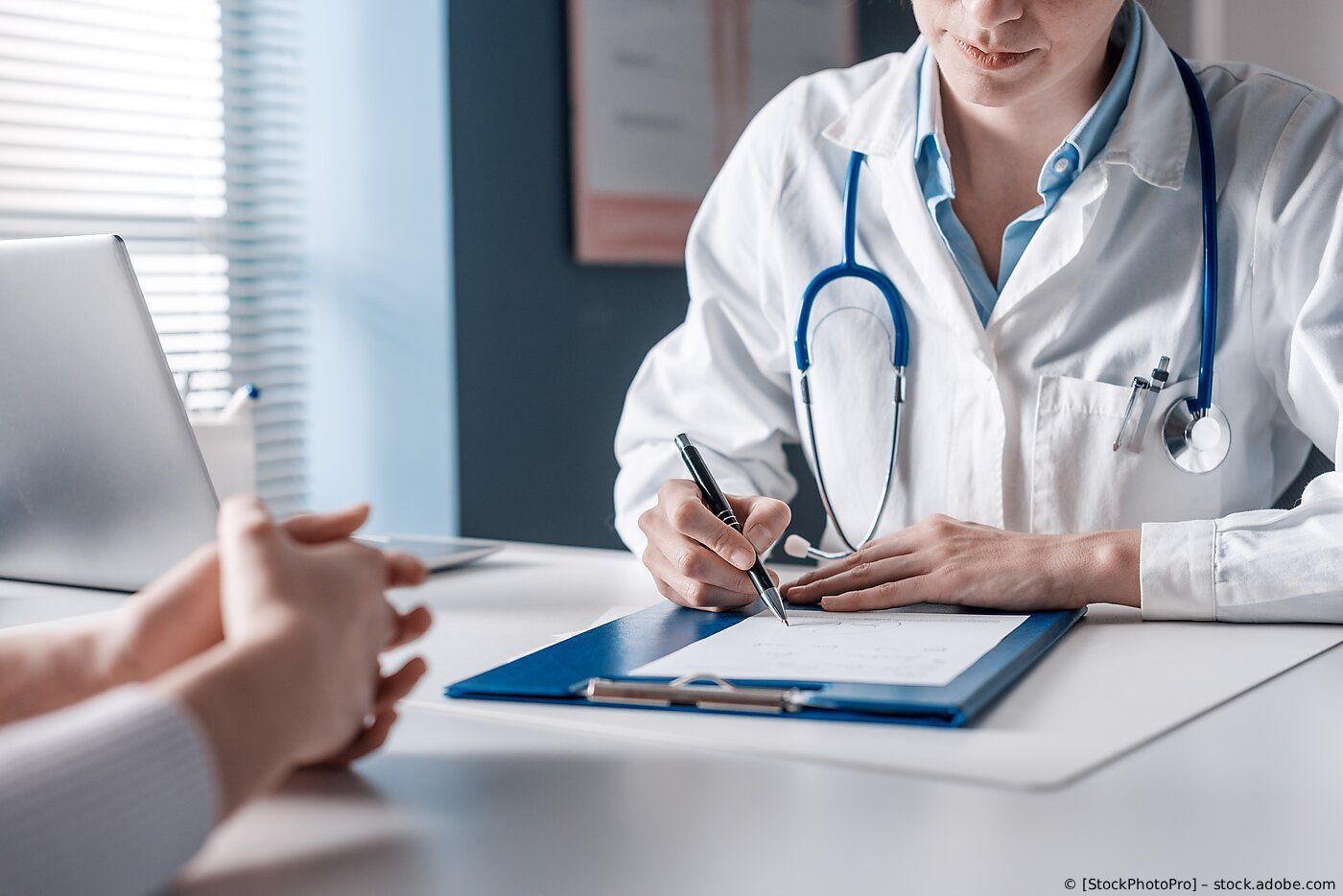Ein Arzt macht sich während einer Patientenkonsultation an einem Schreibtisch Notizen; 
