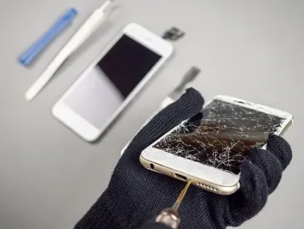 Una persona sostiene un teléfono celular roto con un destornillador en la mano.