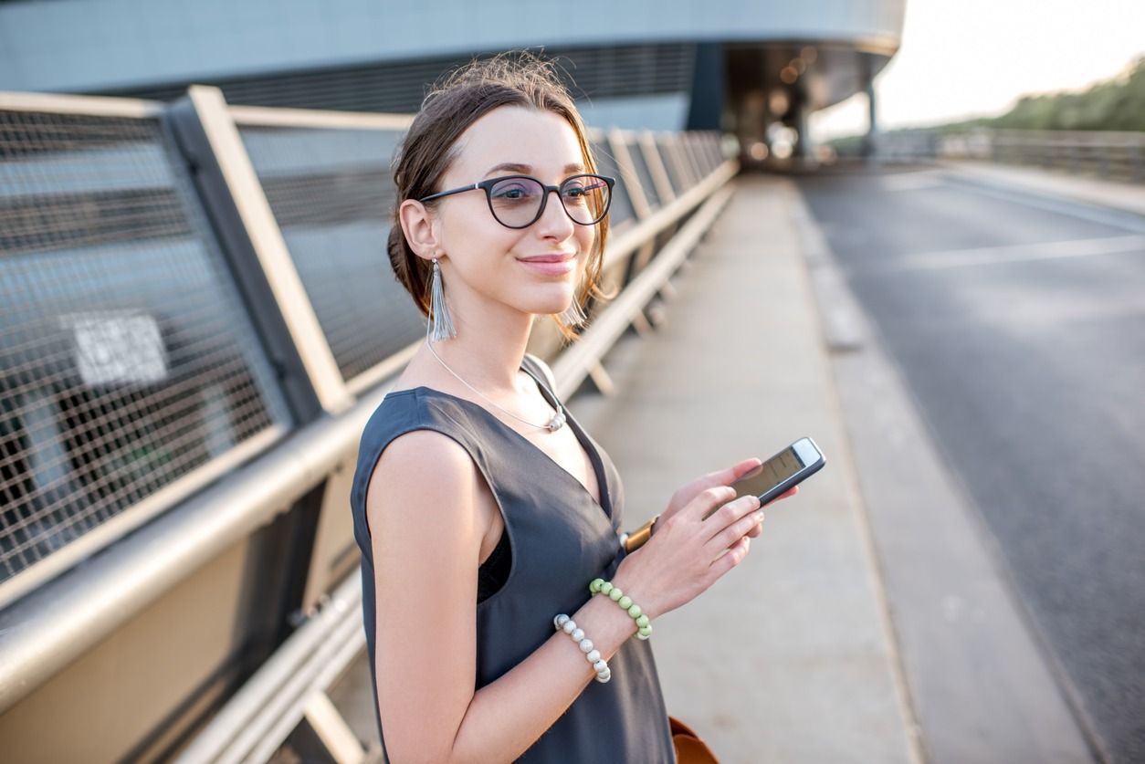 Una mujer que lleva gafas está parada en un puente sosteniendo un teléfono celular.