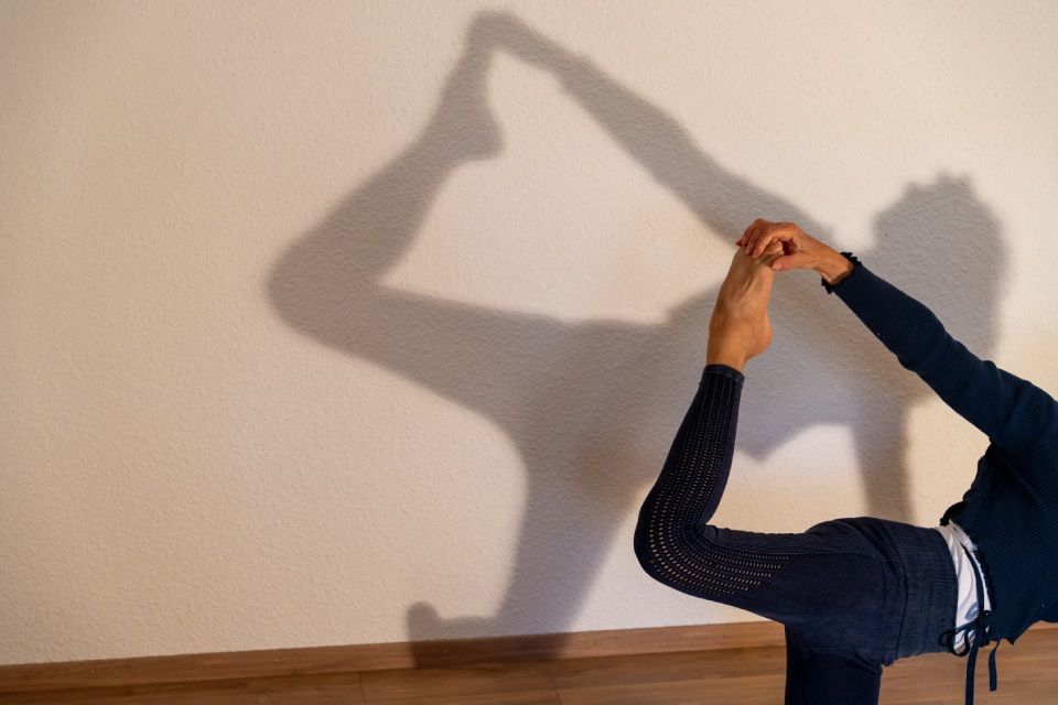 Personne pratiquant le yoga, le dos cambré, la jambe et la main levées, projetant une grande ombre sur le mur.