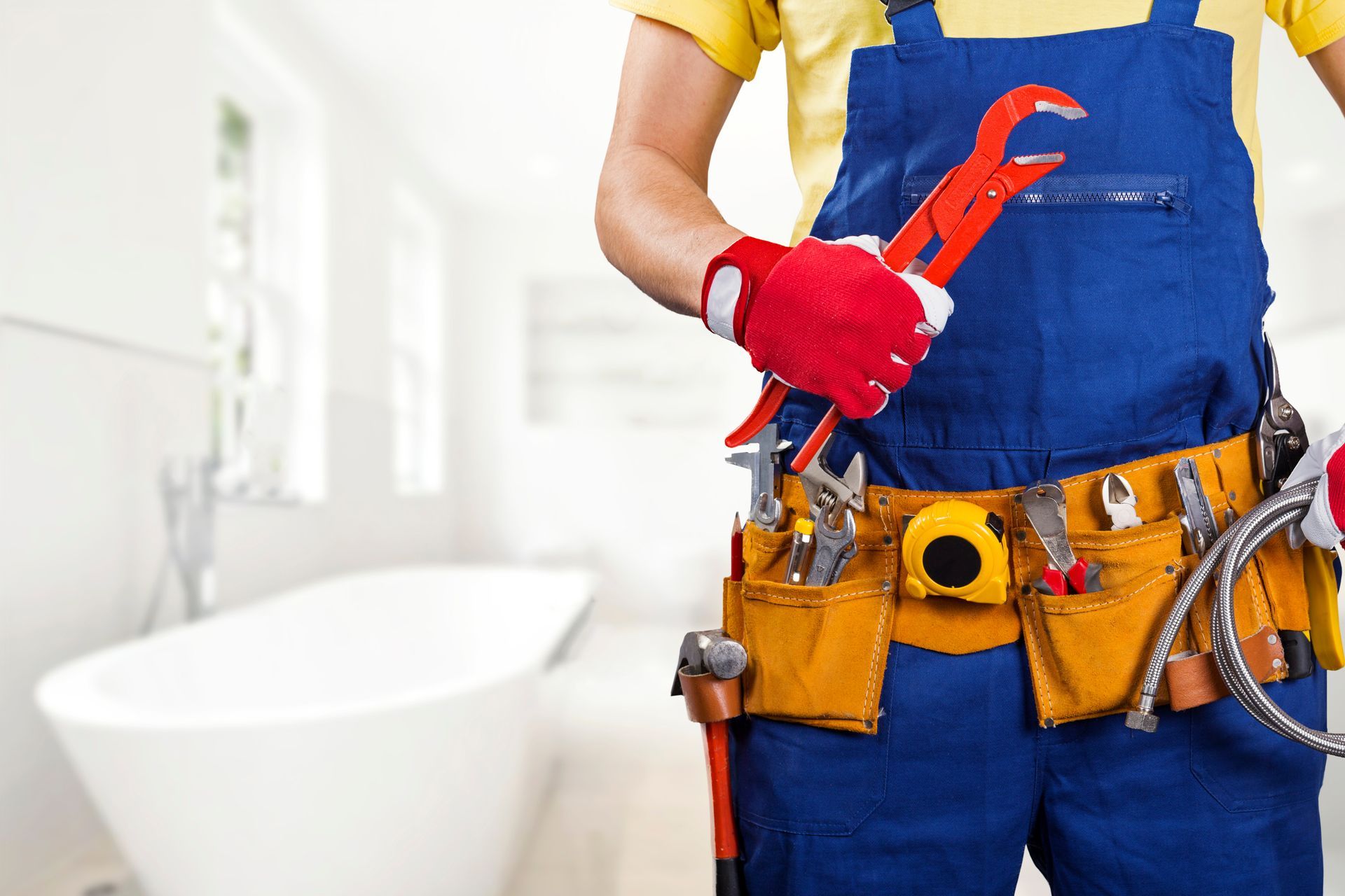 Plombier en salopette bleu et ceinture de travail à la taille tenant une pince dans la main