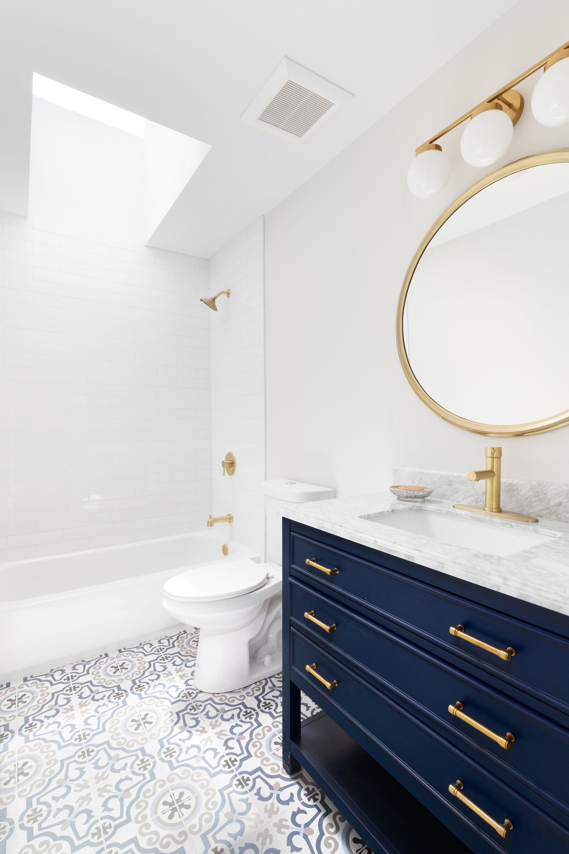Salle de bains avec meuble vasque bleu, toilettes et carrelage au sol imitation carreaux de ciment
