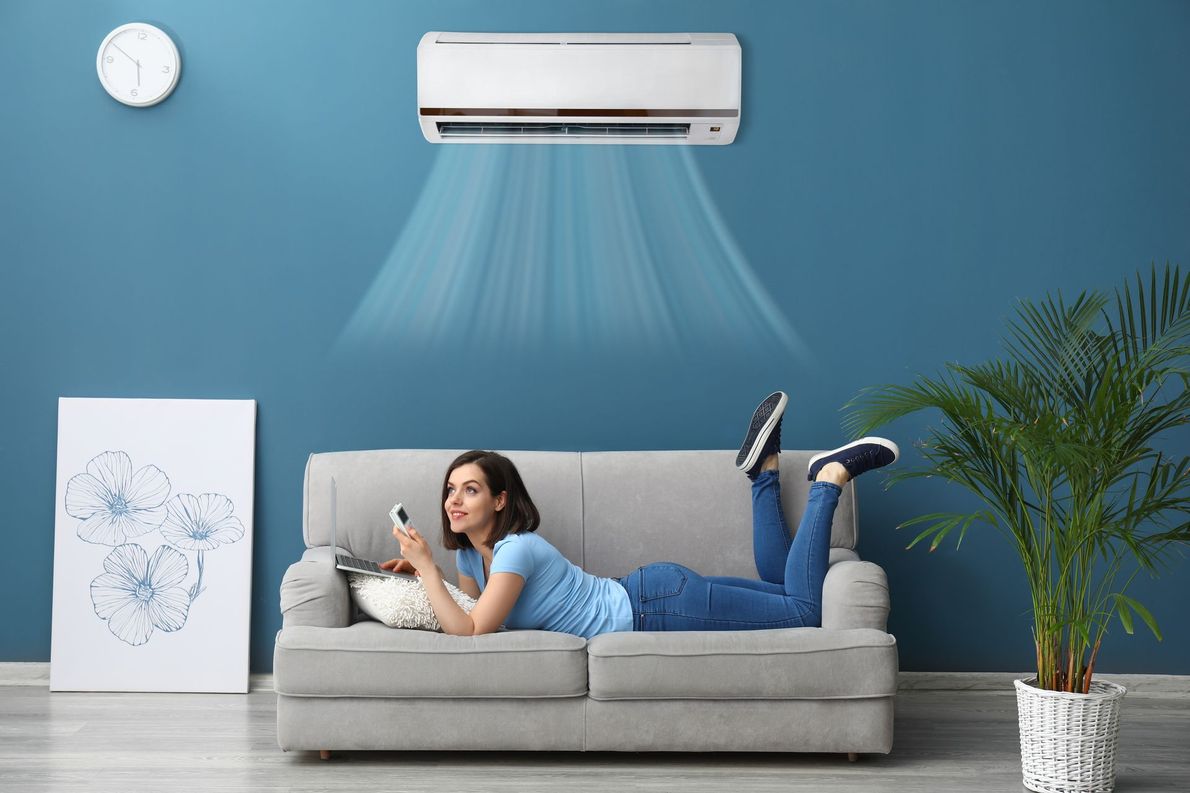 Femme allongée sur un canapé activant son climatiseur à l'aide d'une télécommande