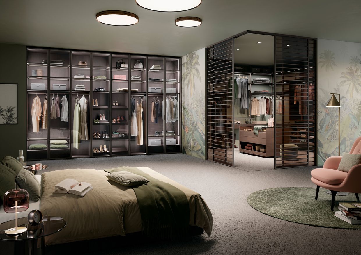 Ein Schlafzimmer mit einem großen Bett und einem begehbaren Kleiderschrank. Raumplus Wohntrend NRW