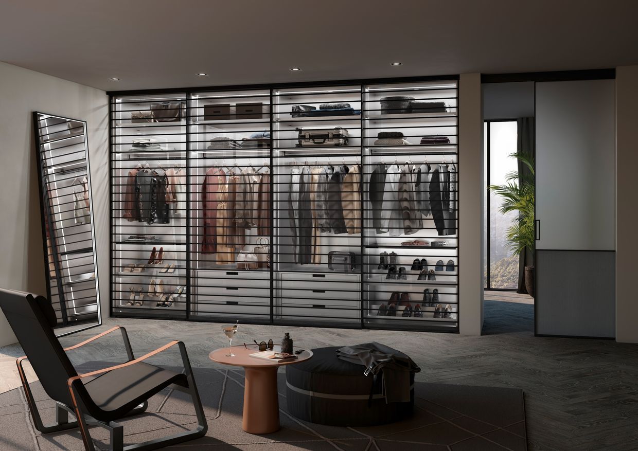 Ein begehbarer Kleiderschrank mit Glasschiebetüren und einem Stuhl. Raumplus Wohntrend NRW