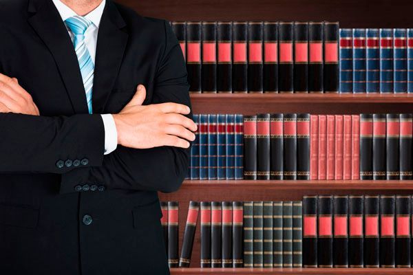 Un hombre con traje y corbata está parado frente a una estantería llena de libros.
