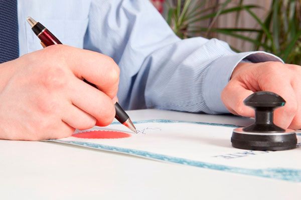 Un hombre está firmando un documento con un bolígrafo y un sello.