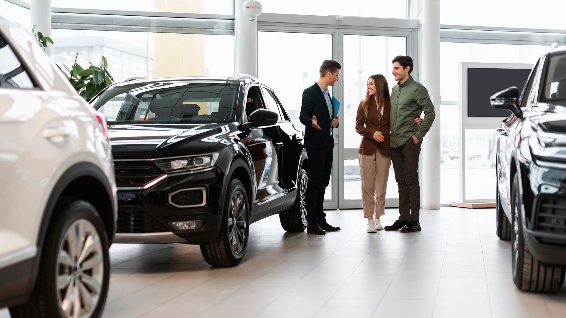 Vendedor de automóviles hablando con una pareja en un concesionario de automóviles, rodeado de vehículos.