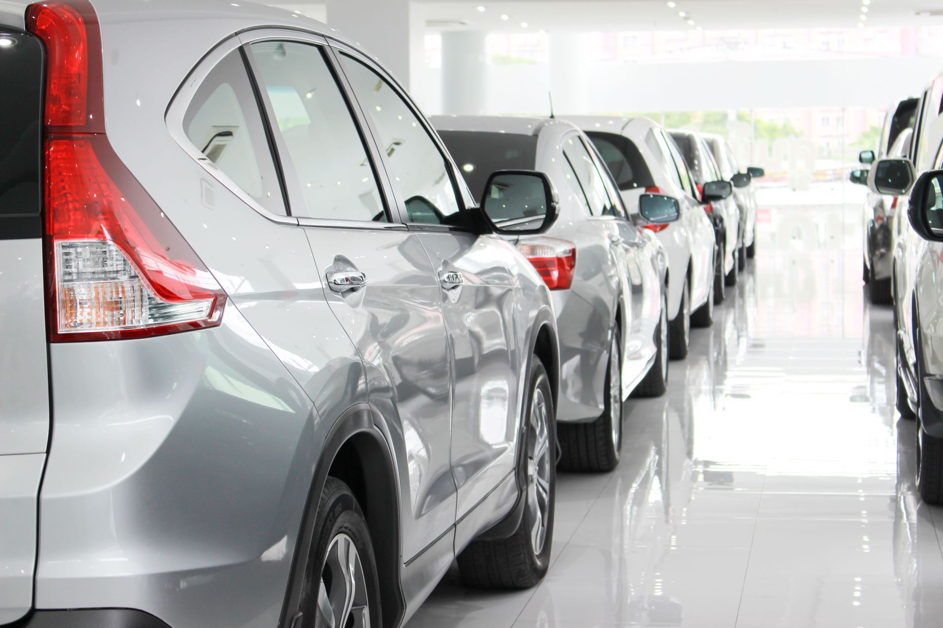 Coches plateados aparcados en una sala de exposición luminosa; varios coches en fila, vista lateral.
