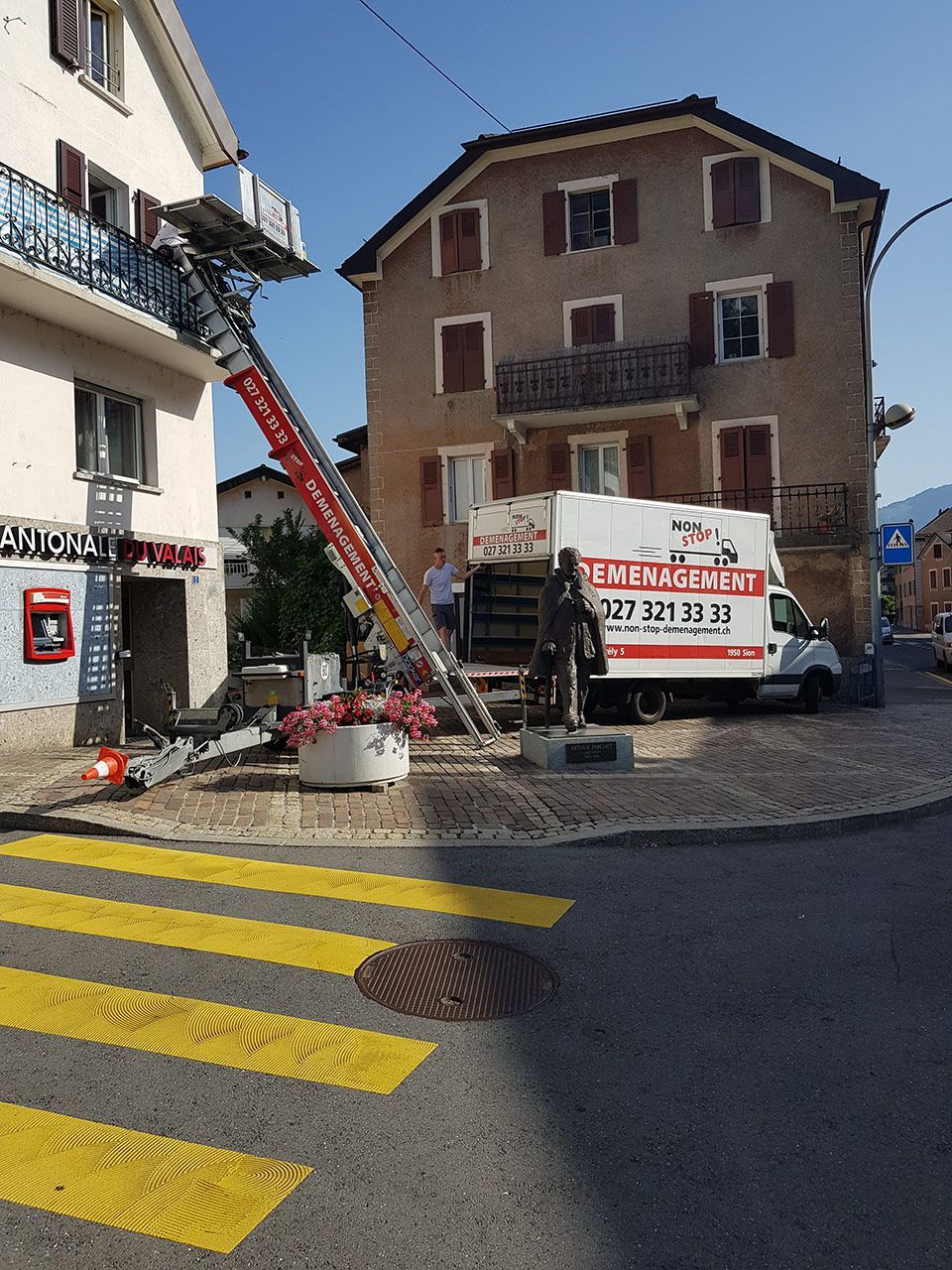 Un camion blanc auquel est attachée une échelle est garé devant un immeuble.