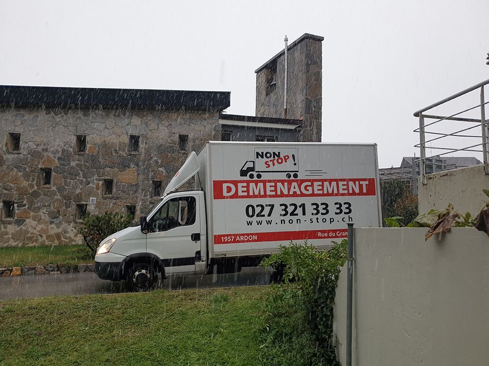 Un camion de déménagement blanc est garé devant un bâtiment en pierre