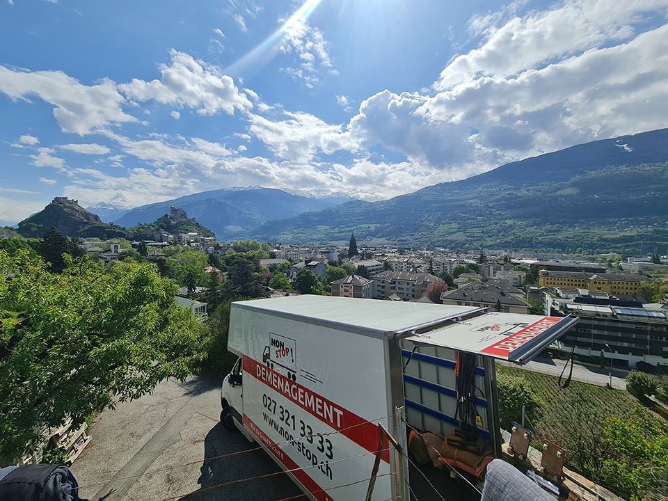 Un camion de déménagement est garé devant une ville avec des montagnes en arrière-plan.