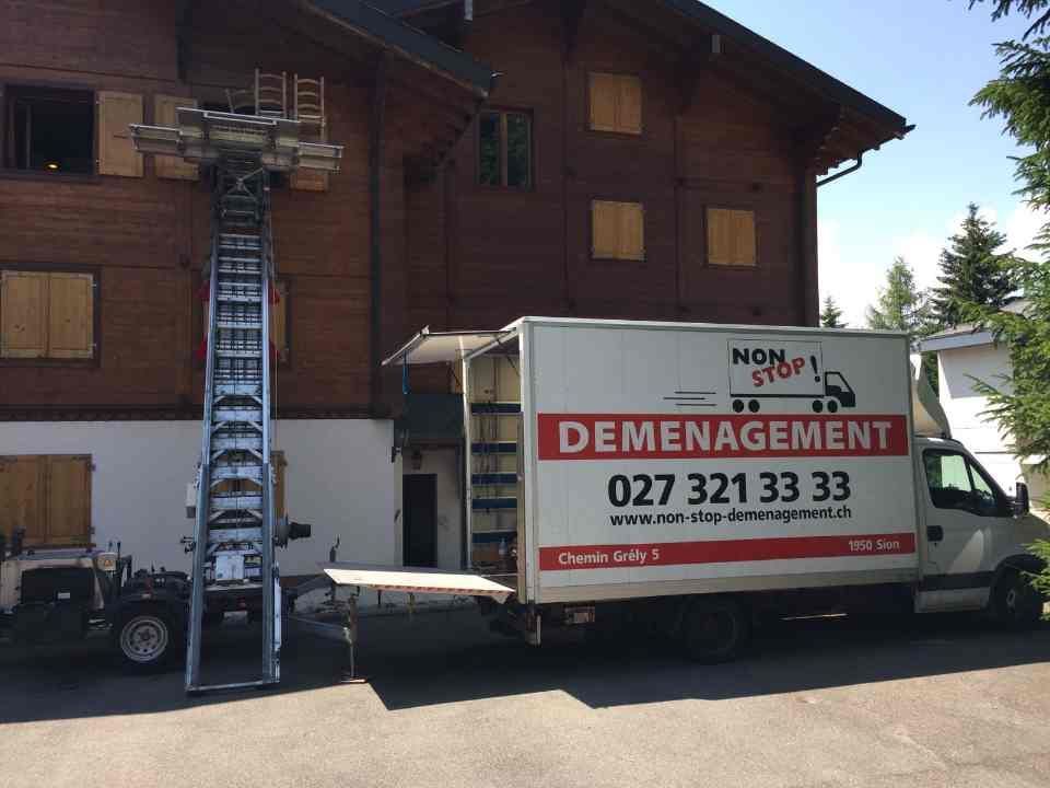 Un camion de Non-Stop déménagement Sàrl est garé devant une maison en bois.