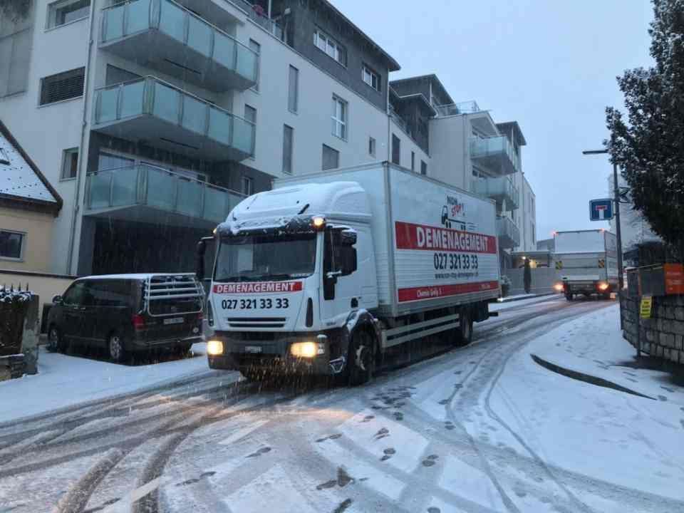 Un camion roule dans une rue enneigée devant un immeuble.
