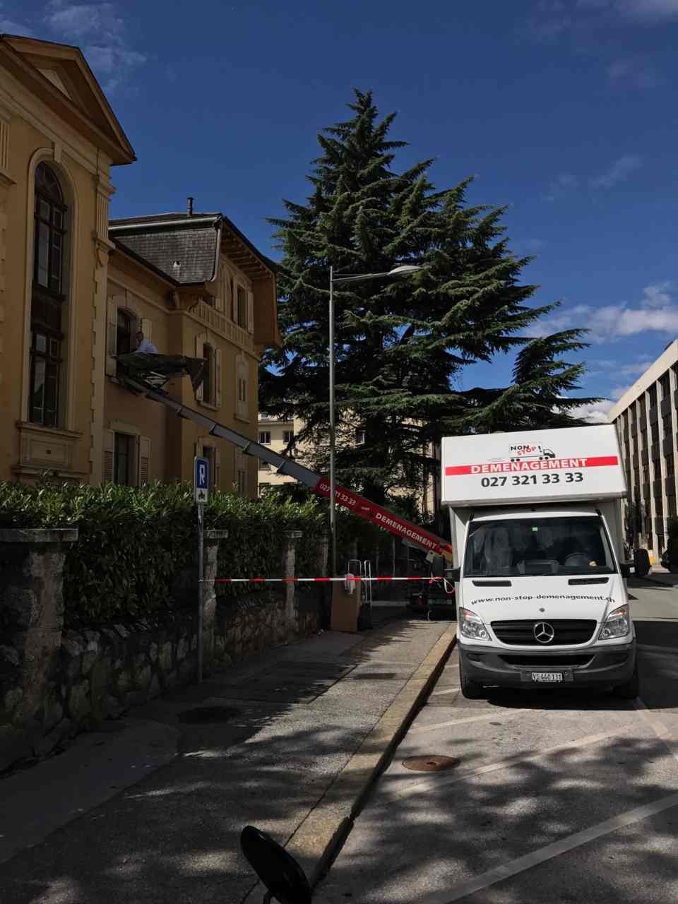Un camion de déménagement est stationné devant un immeuble auquel est attachée une échelle.