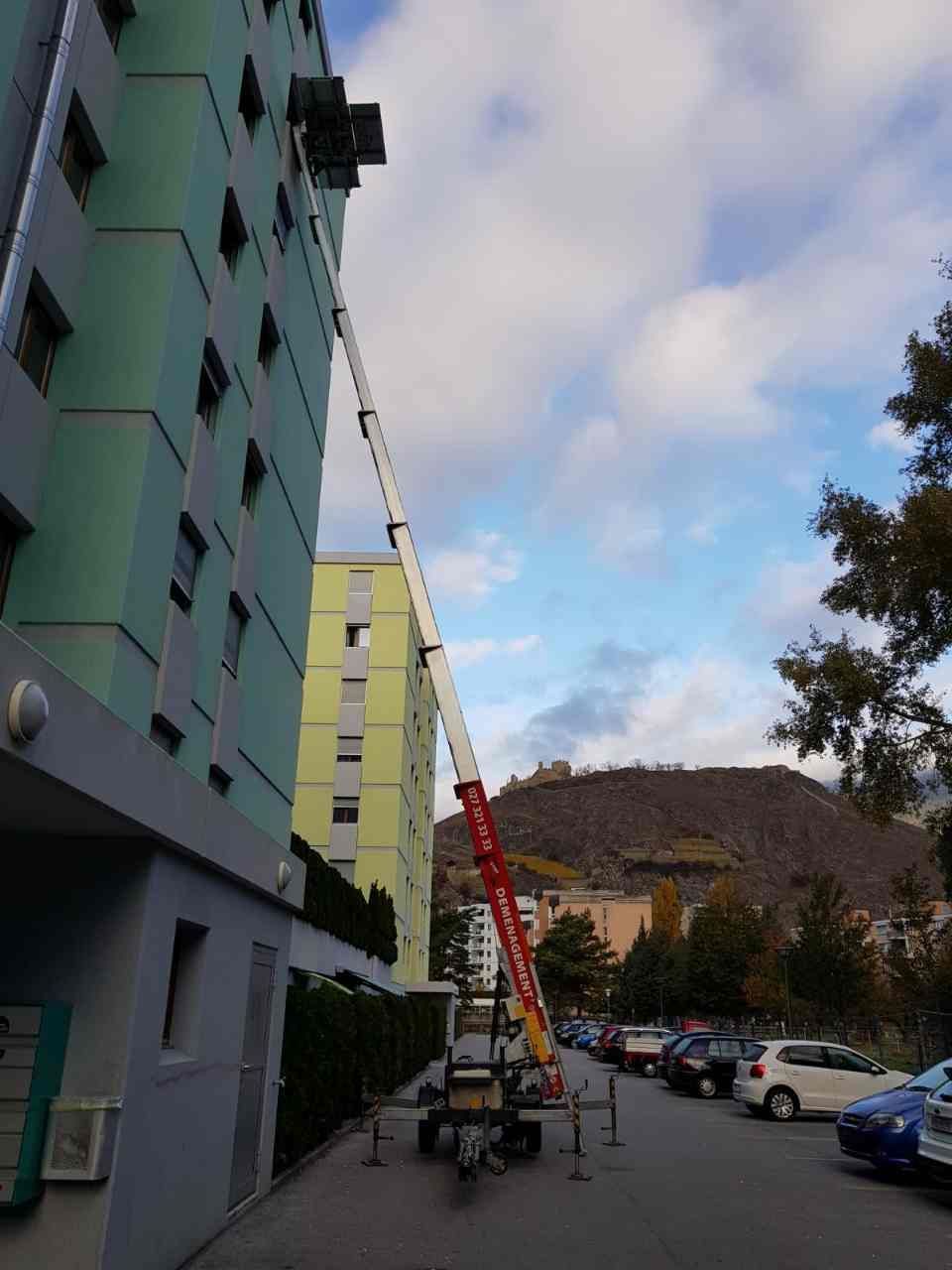 Une échelle est utilisée pour soulever une boîte au sommet d'un bâtiment.