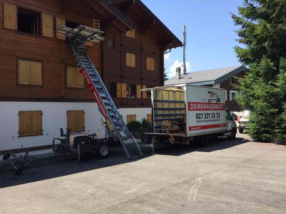 Un camion blanc avec une échelle fixée à l'arrière est garé devant un bâtiment en bois.