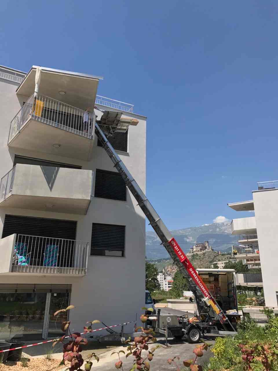 Une grue soulève un balcon au sommet d'un immeuble.