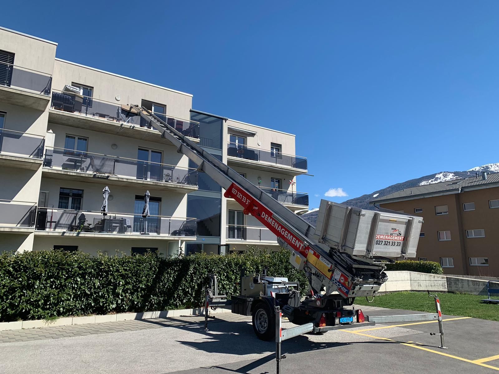 Une grande grue est garée devant un immeuble.