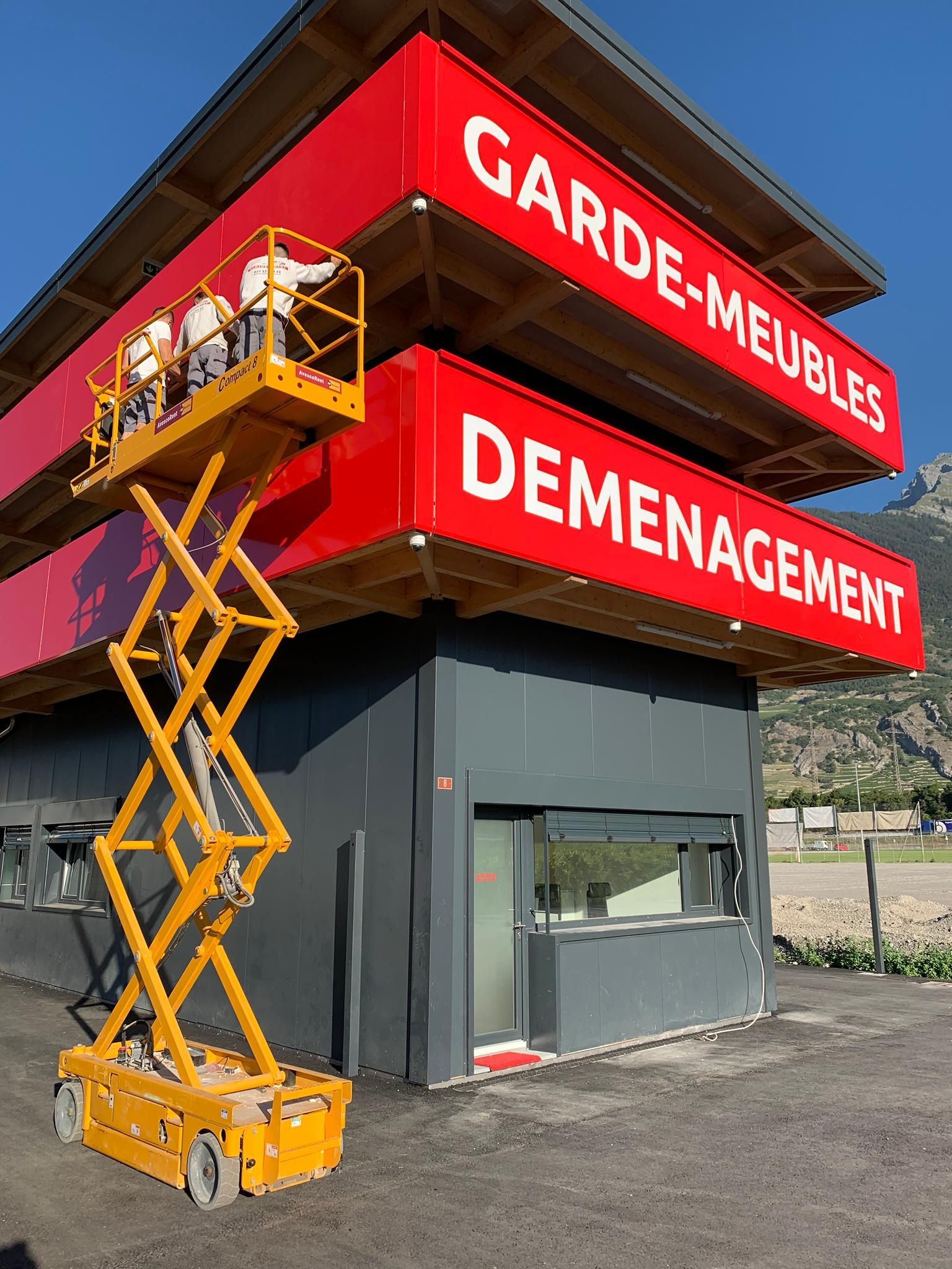 Un ascenseur à ciseaux jaune se trouve devant un bâtiment qui dit déménagement