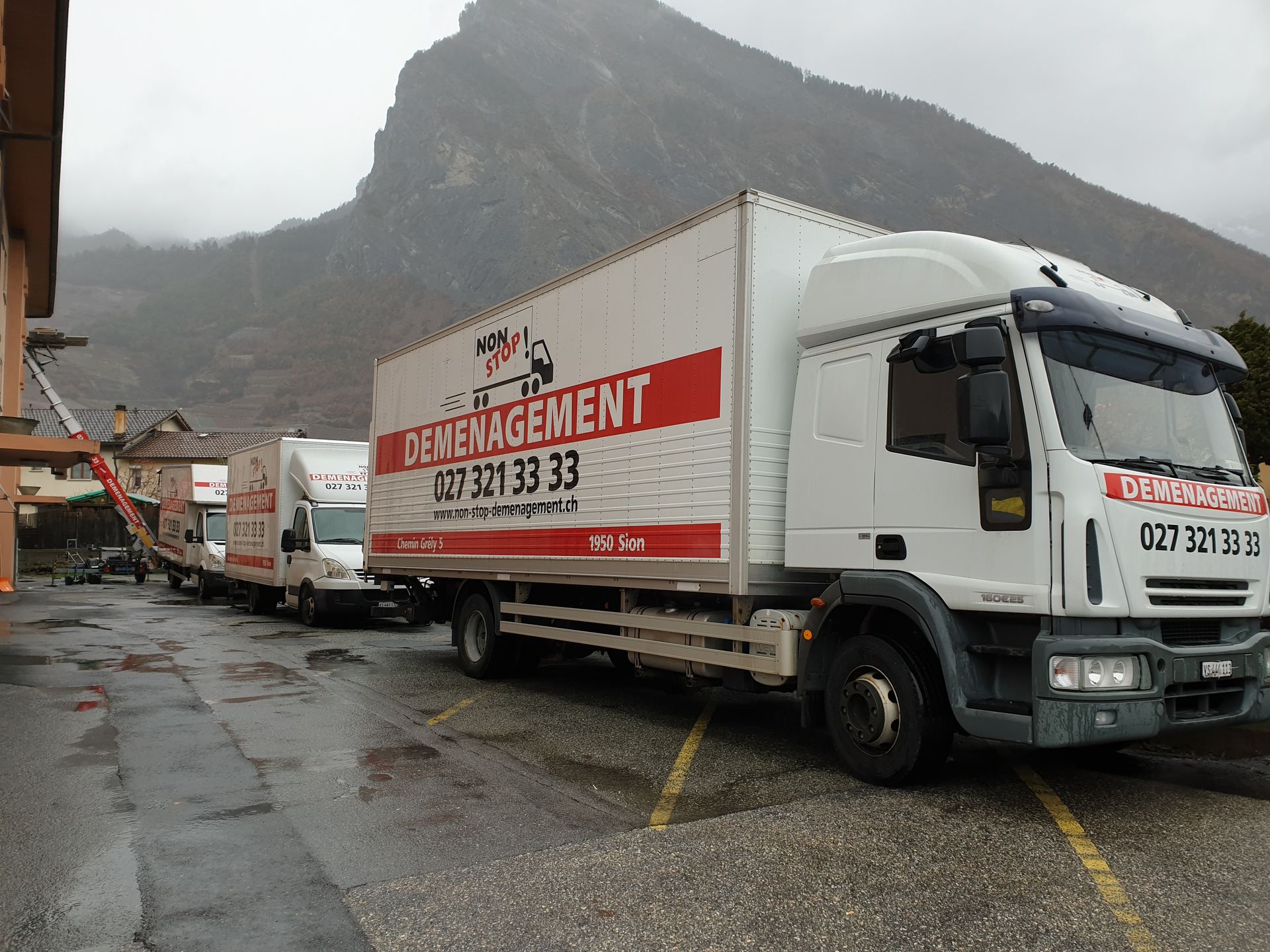 Une rangée de camions de déménagement sont garés dans un parking avec une montagne en arrière-plan.