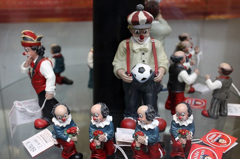 Eine Gruppe Clowns sitzt mit Blumen und einem Fußball in den Händen auf einem Tisch.