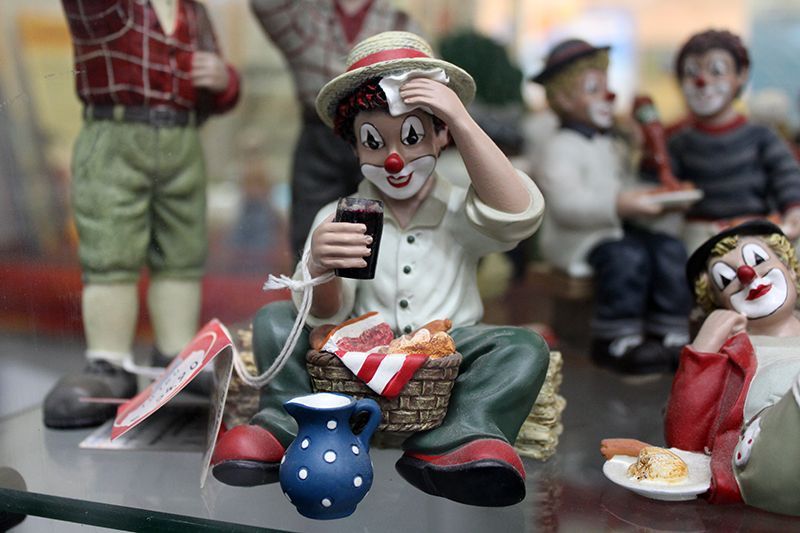 Eine Clownfigur sitzt mit einem Korb voller Essen und einem Krug Milch auf einem Tisch.