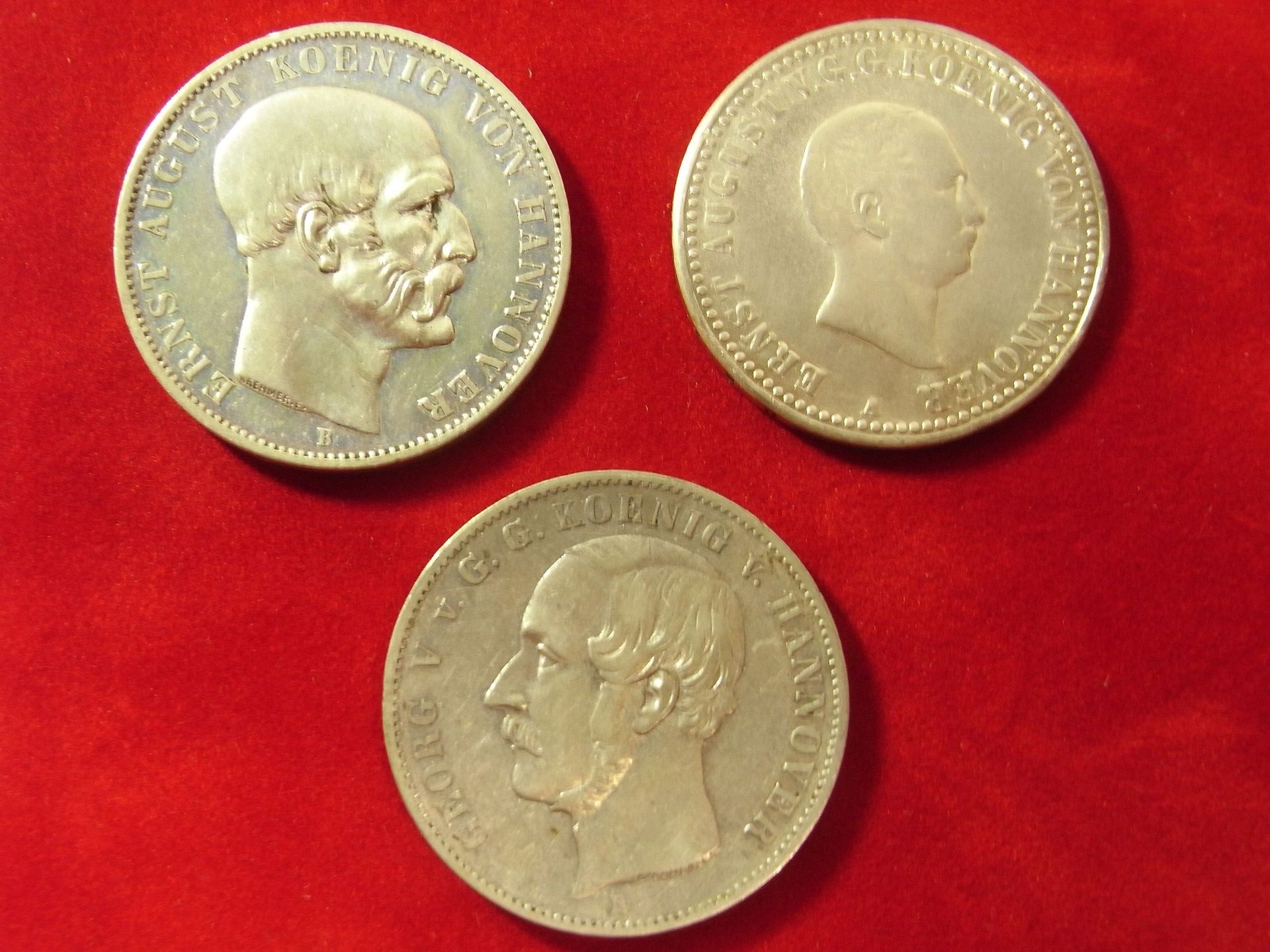 Drei Münzen auf einer roten Fläche, eine davon mit der Aufschrift „Louis“ darauf