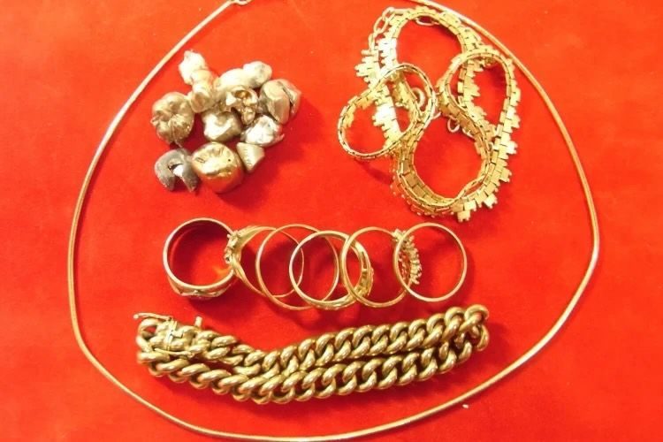 Silbernes Besteck liegt neben goldenen Armbändern und anderen Gegenständen auf einem roten Tuch bei einem Händler für Goldankauf.