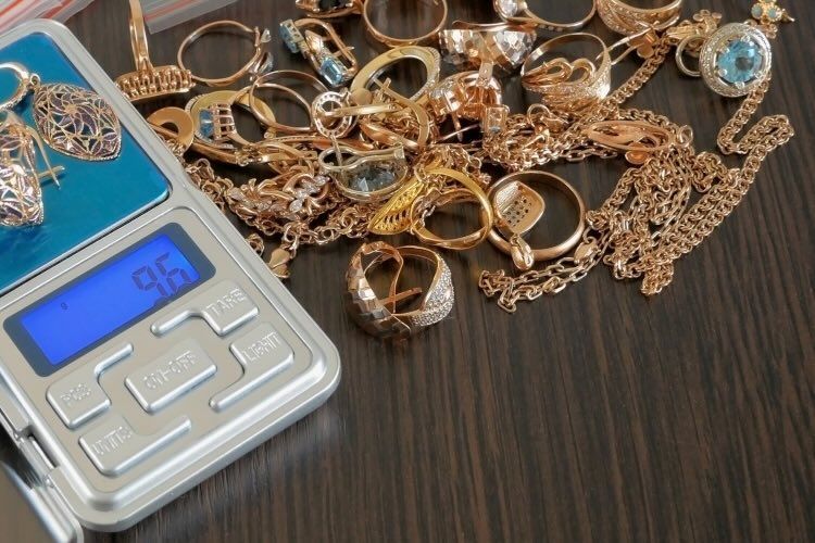 Goldene Ringe und Ketten liegen auf einem Holztisch und daneben liegt ein silberner Rechner für den Goldankauf.