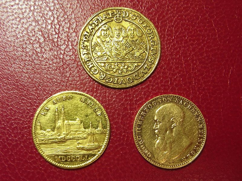 Drei Goldmünzen auf einer roten Fläche, eine davon mit einer Krone darauf