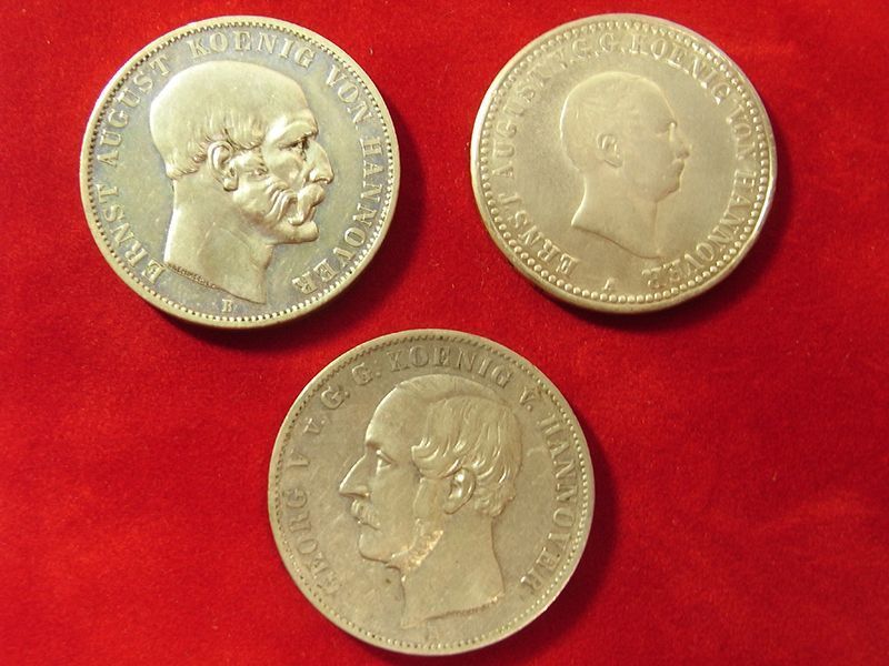 Drei Münzen auf einer roten Fläche, eine davon mit der Aufschrift „Louis“ darauf