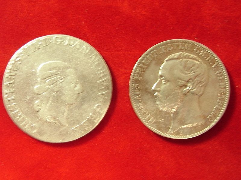 Zwei Silbermünzen auf einer roten Fläche, eine davon trägt das Wort Friedrich