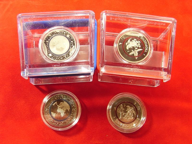 Vier Münzen in durchsichtigen Plastikhüllen auf einer roten Fläche