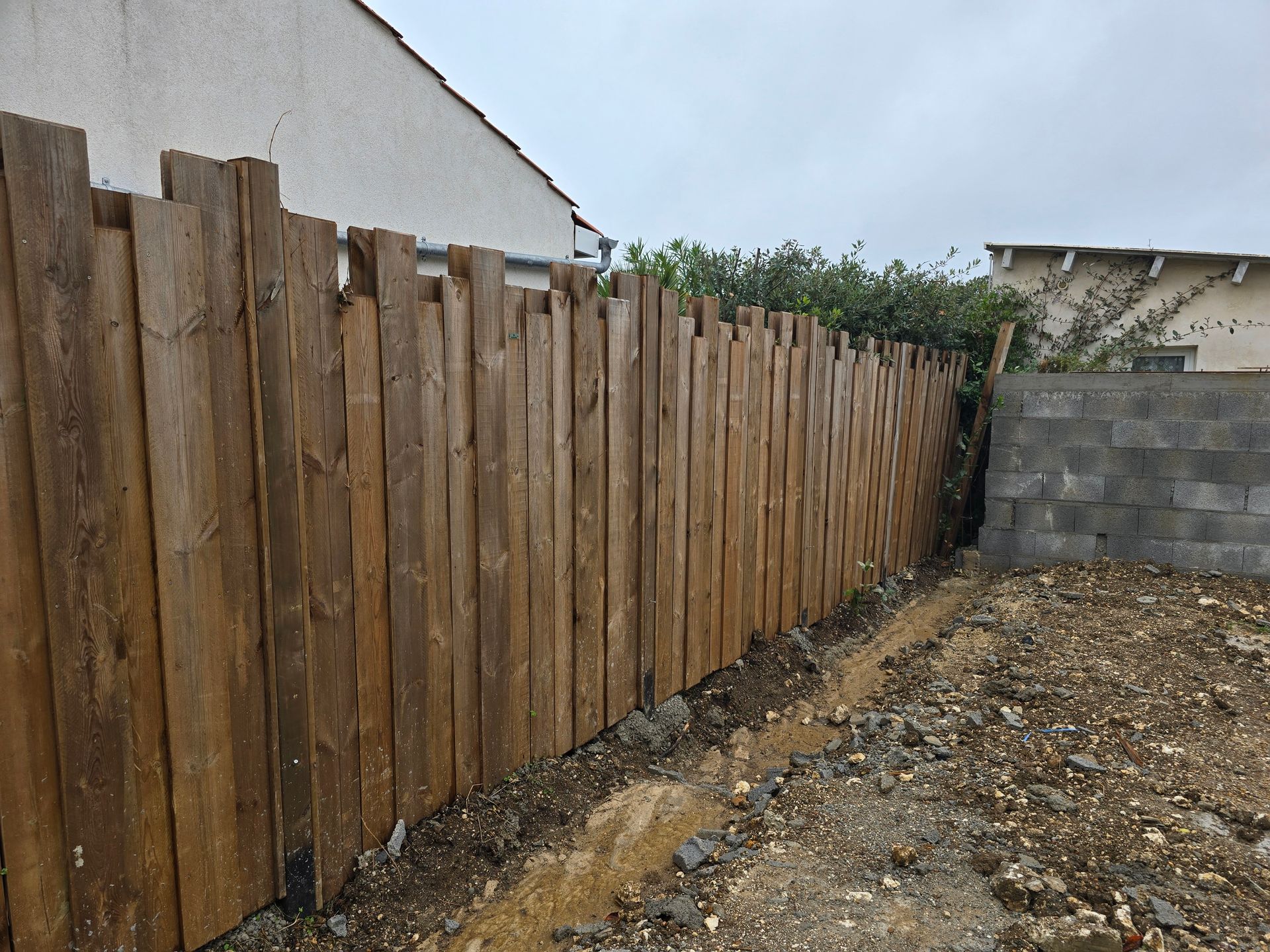 Une clôture en bois sur le côté et un mur en parpaings en fond du terrain