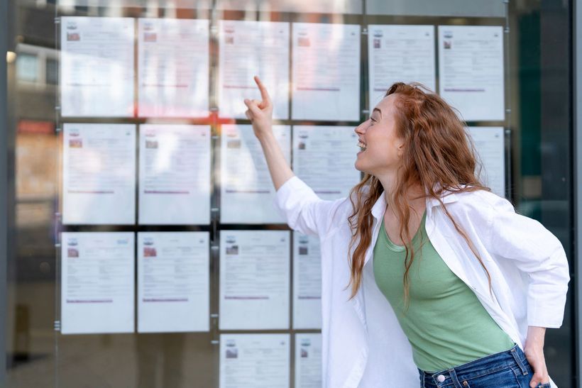 Une dame devant une vitrine d'agence immobilière regardant les offres immobilières.