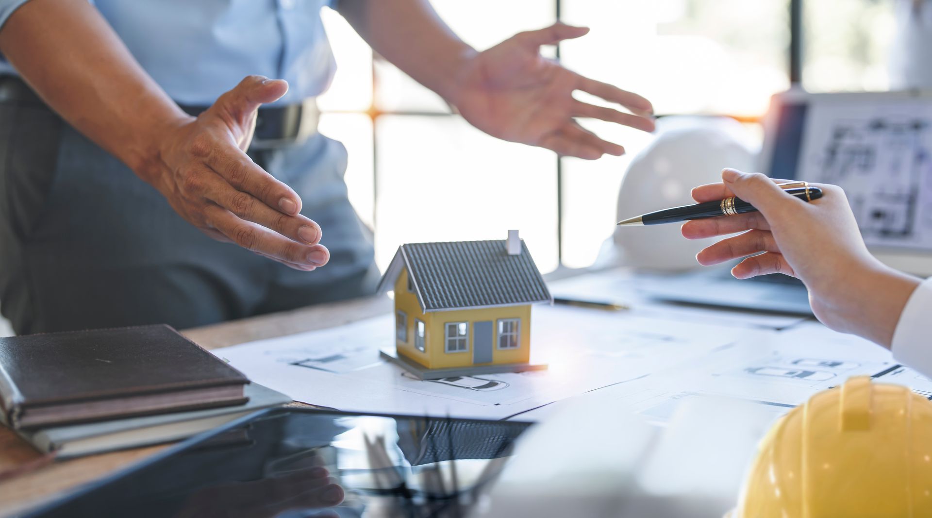 Un homme debout tendant les bras sur une maquette de maison pour un achat immobilier.