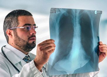 Médico examinando una radiografía de tórax en un entorno médico, con gafas y estetoscopio.