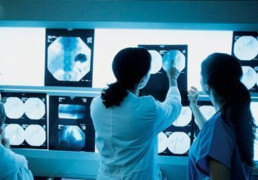 Profesionales médicos examinando radiografías iluminadas sobre un panel de luz, en un entorno médico.