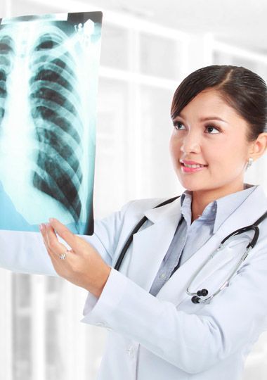 Médico examinando una radiografía de tórax, con bata blanca y estetoscopio.