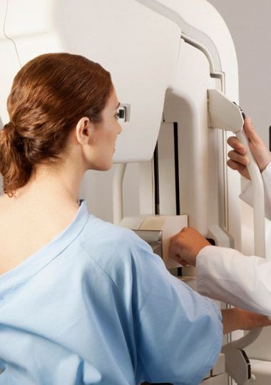 Mujer sometiéndose a una mamografía, asistida por una persona con bata blanca, en un entorno médico.