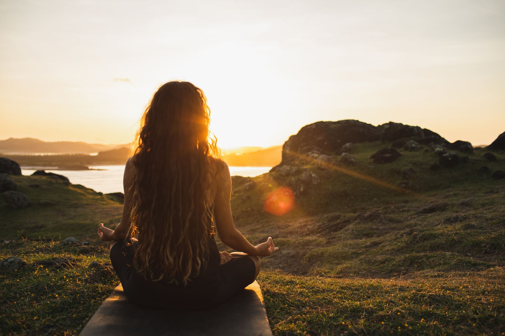 Une femme est assise sur un tapis de yoga et regarde le coucher du soleil.