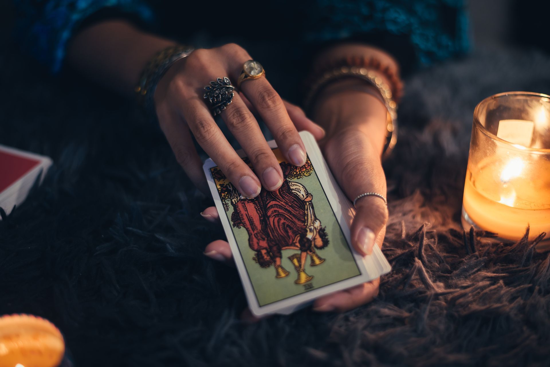 Une femme tient une carte de tarot dans ses mains à côté d'une bougie.