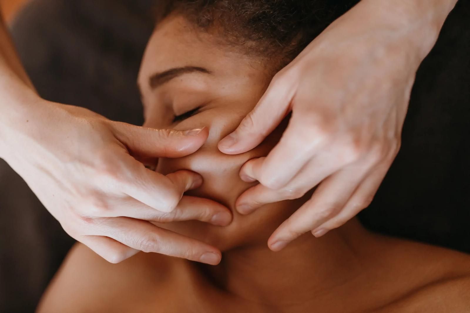 Des mains massent le visage d'une personne détendue, les yeux fermés.