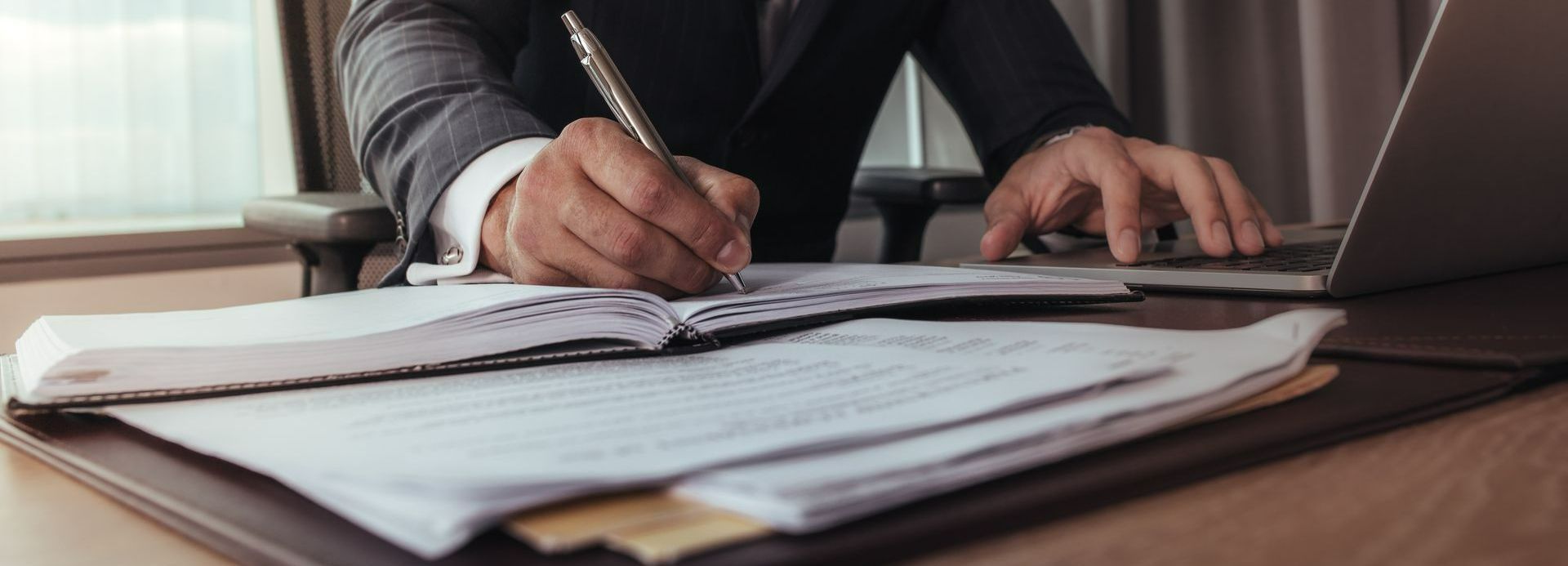 Homme écrivant dans un cahier et utilisant son ordinateur en même temps