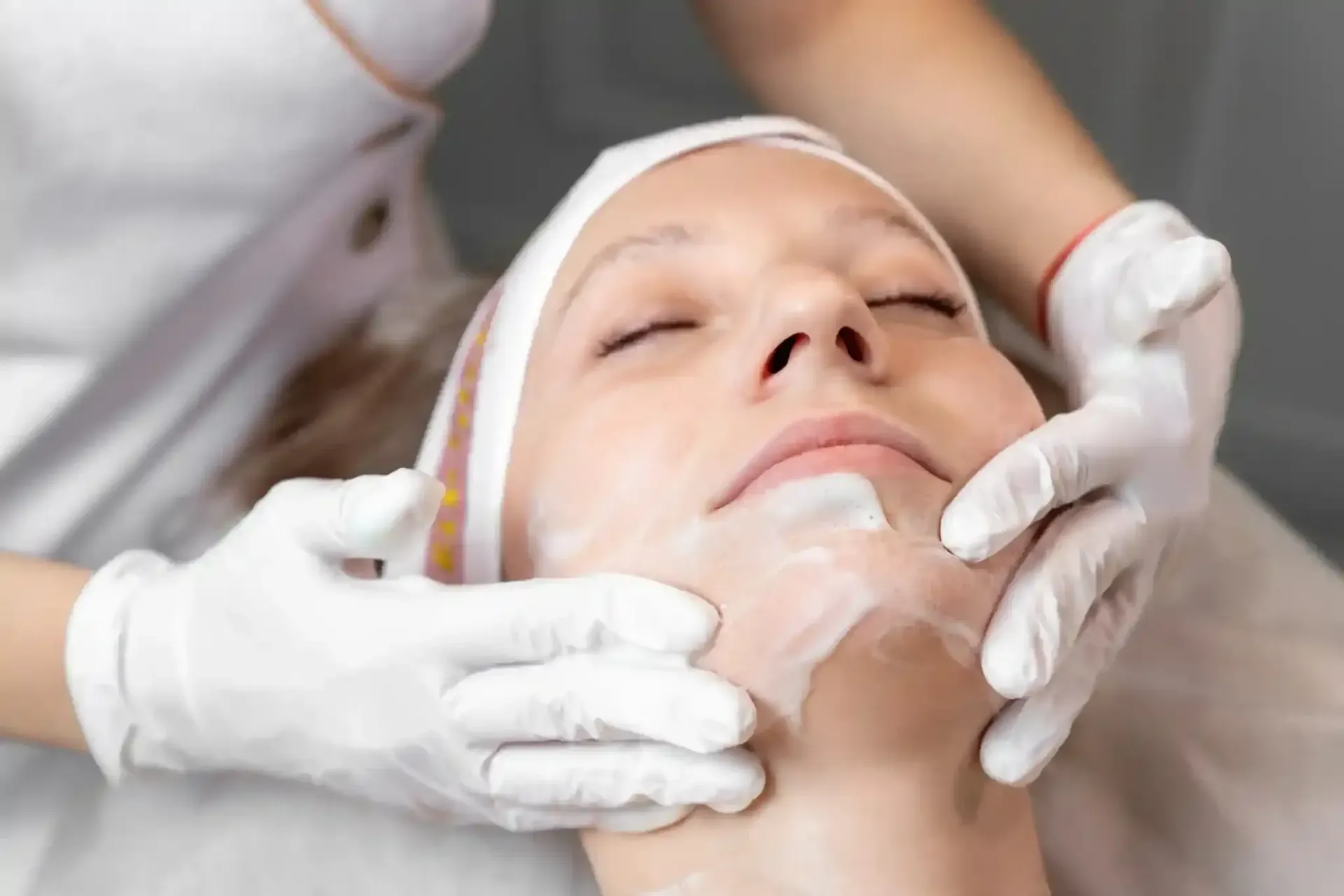 Persona recibiendo tratamiento facial; manos en guantes aplicando crema.